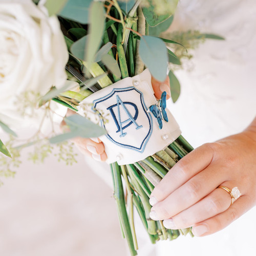 Custom embroidered wedding crest on a ribbon that is used to wrap the bride's flower bouquet on her wedding day. The monogram is embroidered in blue.