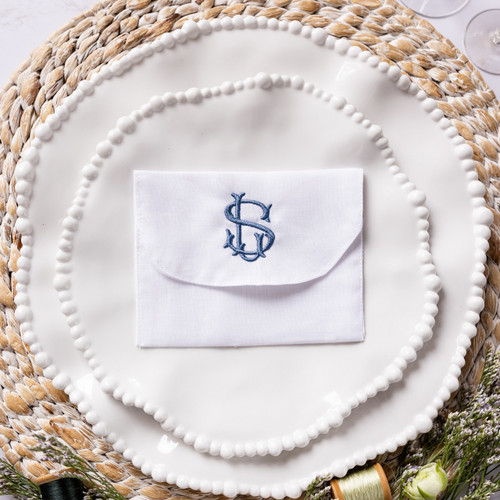 Custom embroidered linen favor envelope. White linen envelope personalized with custom monogram in smokey blue embroidery thread. Favor envelope is perfect for chocolates, donation certificate or gift card. Shown on white salad and dinner plates with flowers.