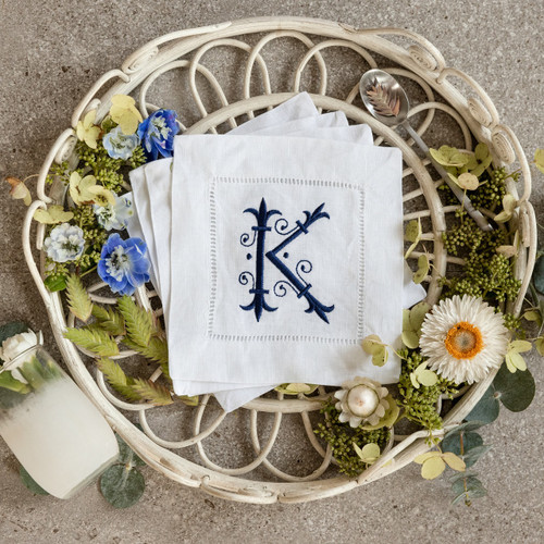 Custom embroidered cocktail napkins. Set of 4. Customized with a monogram initial in navy thread. Background has flowers, a glass and a spoon.