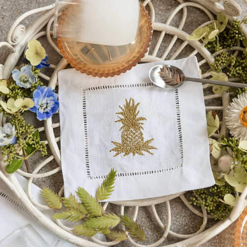 Custom embroidered cocktail napkins. Set of 4. Embroidered with a pineapple in metallic gold thread. Background has a basket, flowers, glass and a spoon.