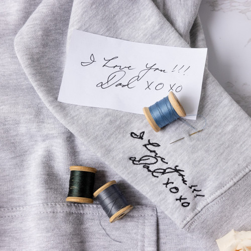 Handwriting embroidered on a sweatshirt hoodie in black thread. Handwritten note shown with embroidered handwriting and decorative threads.