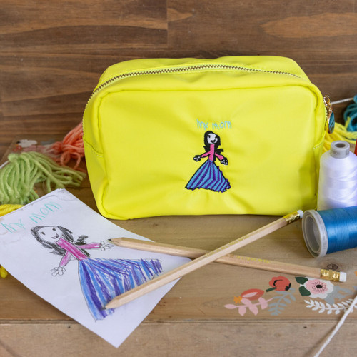 Custom embroidered bag personalized with your child's drawing. Drawing embroidery is done in black, purple, blue and pink threads. Bag is shown on a wood table with flowers and embroidery threads.