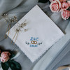Something Blue Handkerchief with initials, wedding date and wedding rings.  It is embroidered in powder blue thread on a handkerchief with white lace trim. 