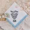 Something Blue handkerchief with embroidered name, date and floral heart. The handkerchief is white with powder blue lace and is shown with other bridal accessories.
