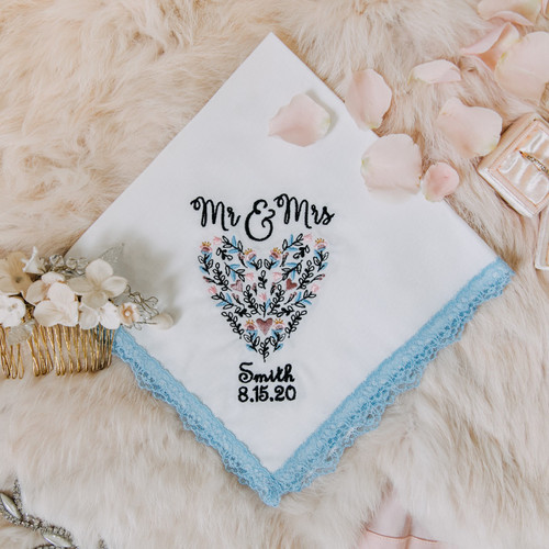 Something Blue handkerchief with embroidered name, date and floral heart. The handkerchief is white with powder blue lace and is shown with other bridal accessories.
