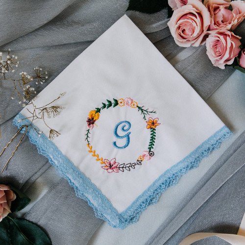 Something Blue handkerchief has embroidered floral wreath & bridal monogram. Handkerchief has blue lace trim & white fabric.
